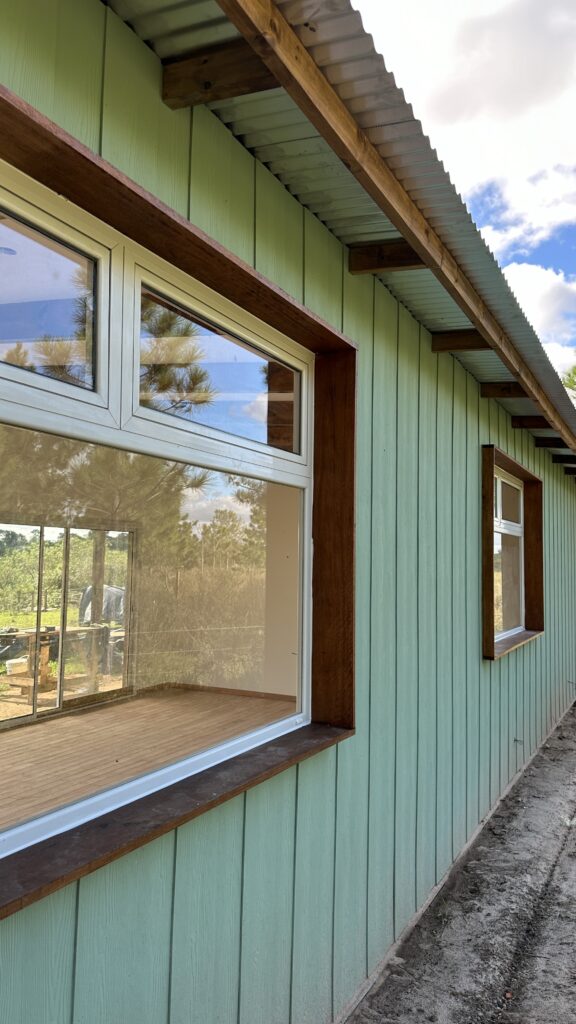 Casa con revestimiento de durlock y vigas a la vista. Aberturas blancas. Piso de madera. Revestimiento de sidding