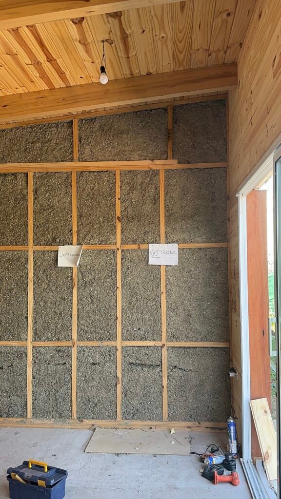Vista interior de un muro en construcción con sistema Wood Frame de B3 Hogar, mostrando la aplicación de celulosa proyectada cubriendo todas las cavidades de la estructura de madera para una aislación térmica y acústica eficiente.